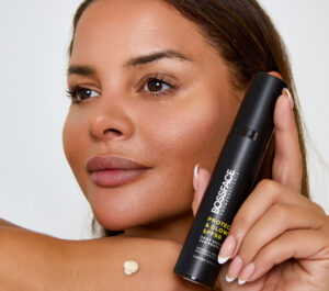 Woman holding Protect and Glow skincare product next to her cheek with cream on the back of her hand