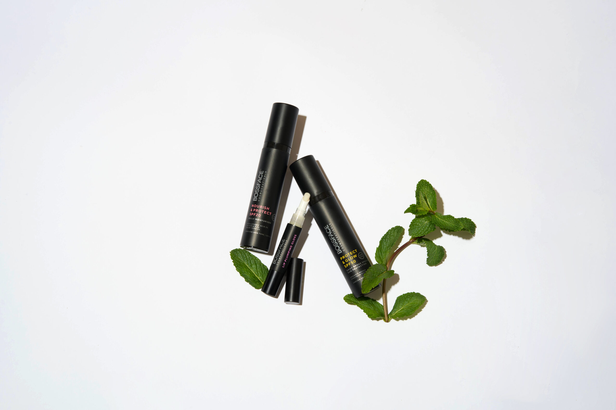 three bossface black skincare bottles lying on a white background with leaves lying beside them
